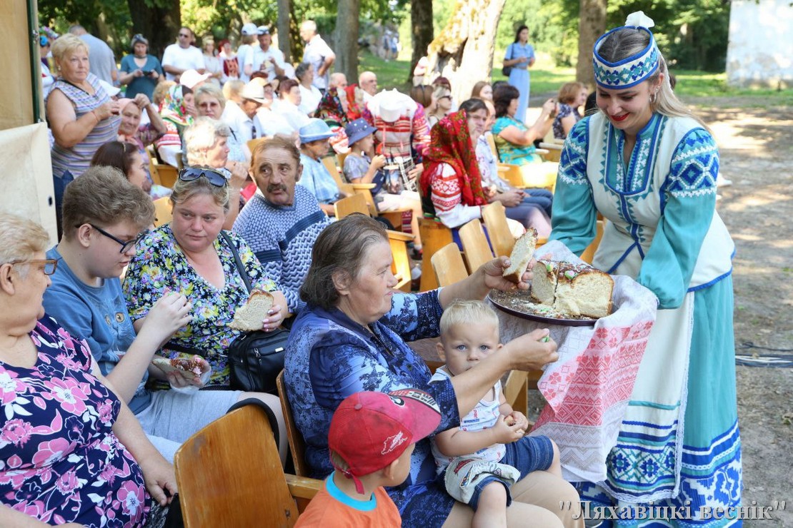Участница фестиваля в народном костюме угощает гостей пирогом.